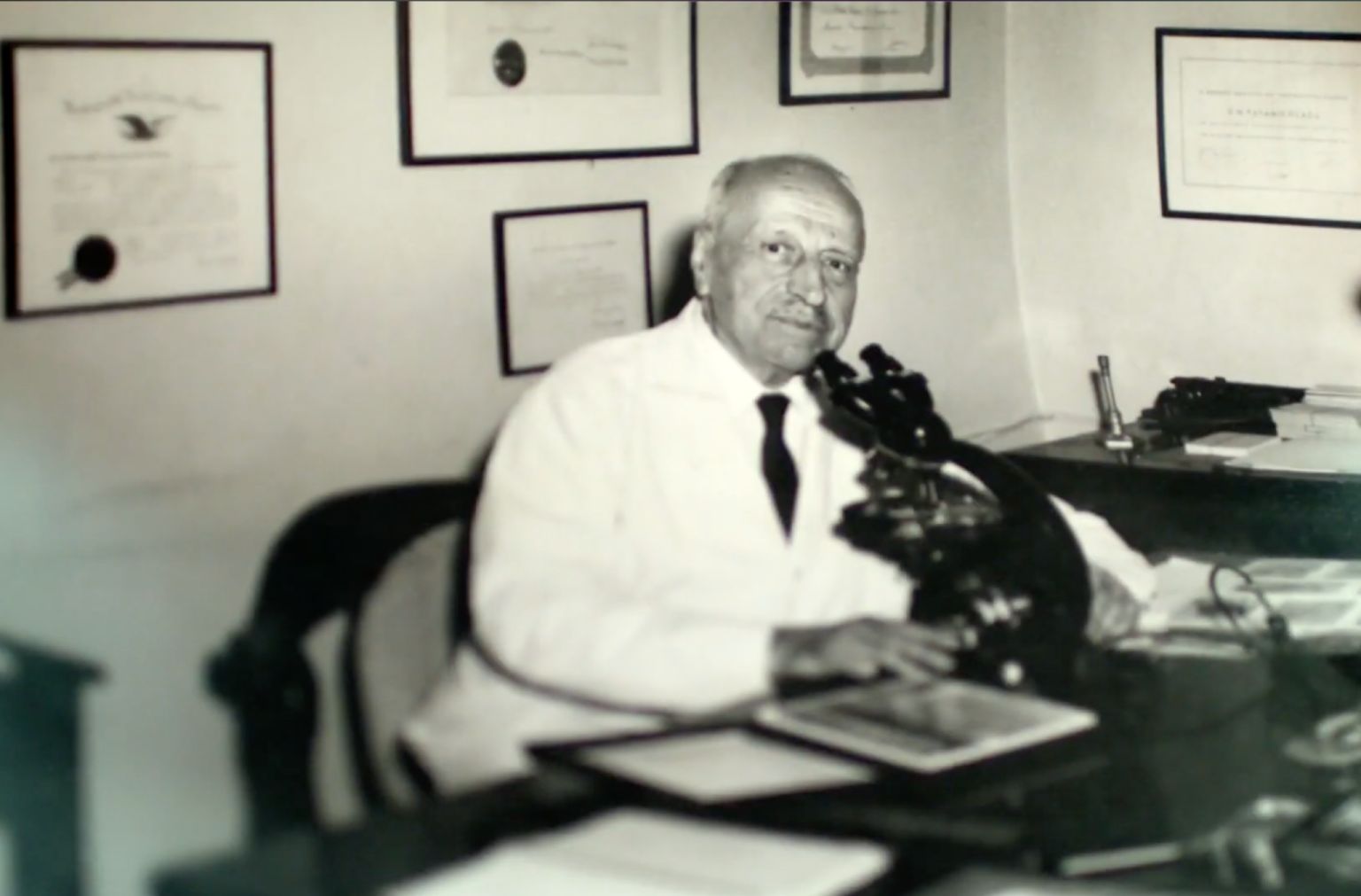 Dr. Papanicolaou at his desk, surrounded by his diplomas and microscope.